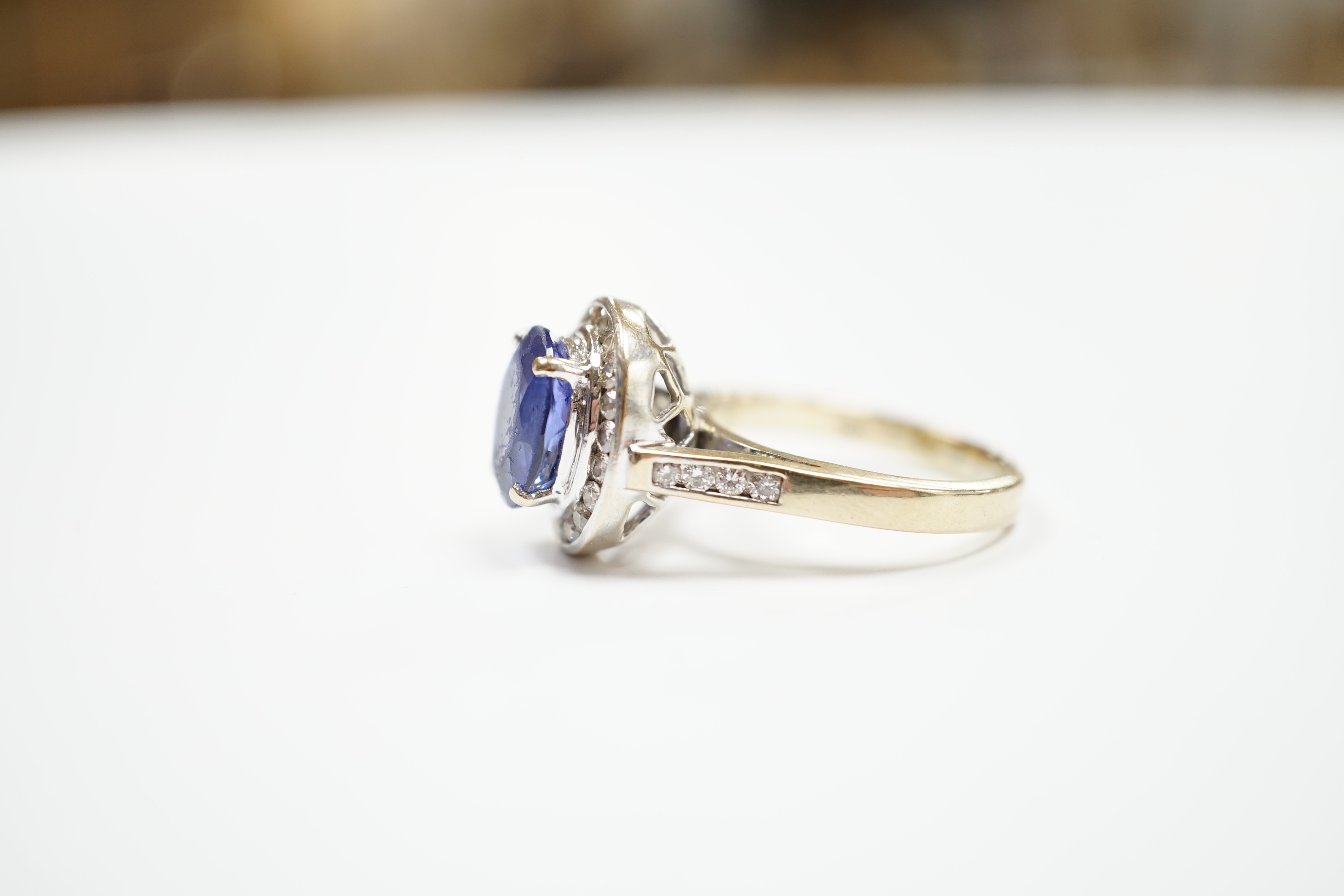 A modern 750 and oval cut single stone tanzanite(worn) set dress ring, with diamond set border and shoulders, size P, gross weight 8.9 grams.